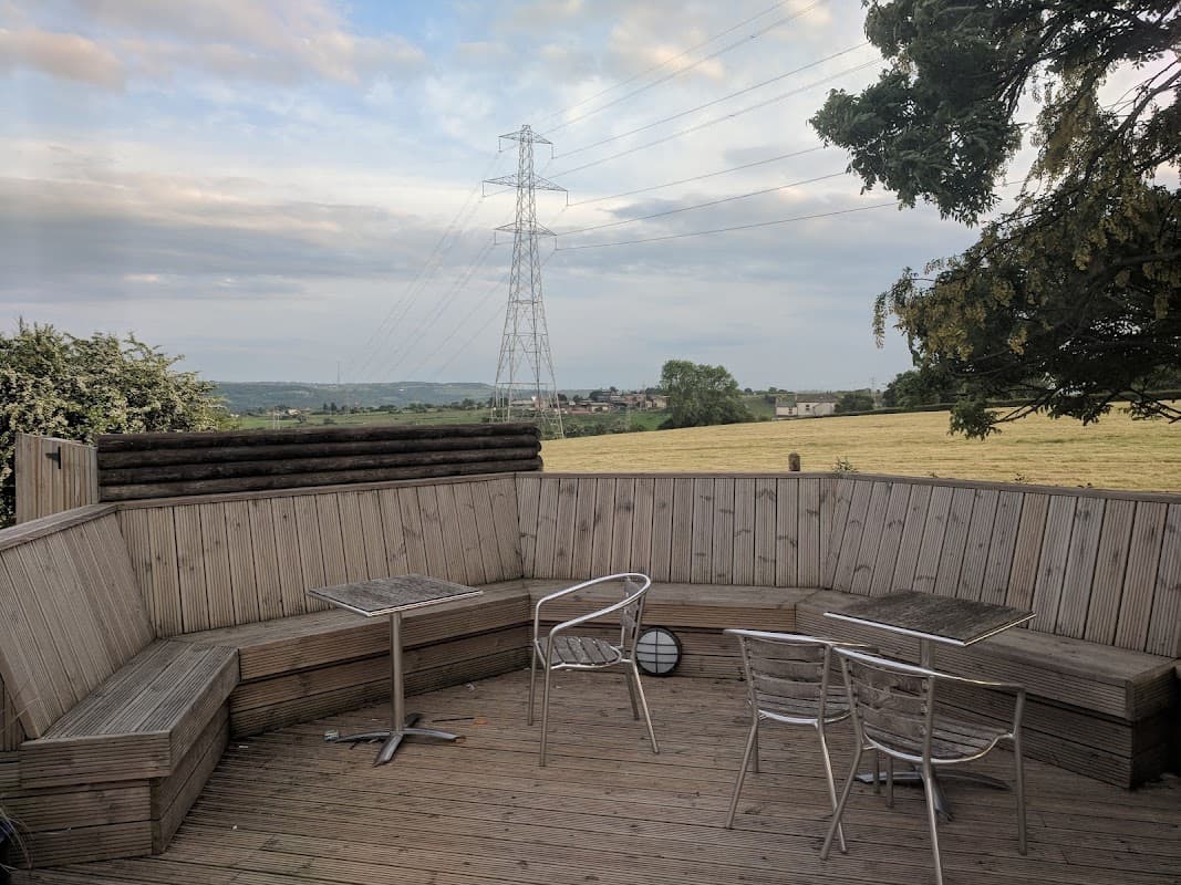 Outdoor seating area with wooden benches and tables, overlooking a grassy field and power lines in the distance.