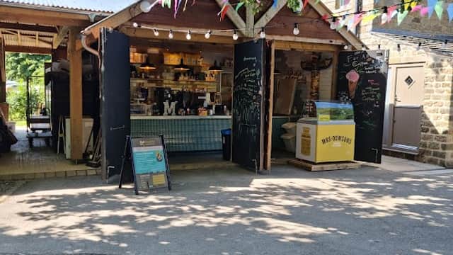 Campsite shop with colorful bunting, outdoor seating, and a menu board under leafy trees in Appletreewick, Yorkshire.