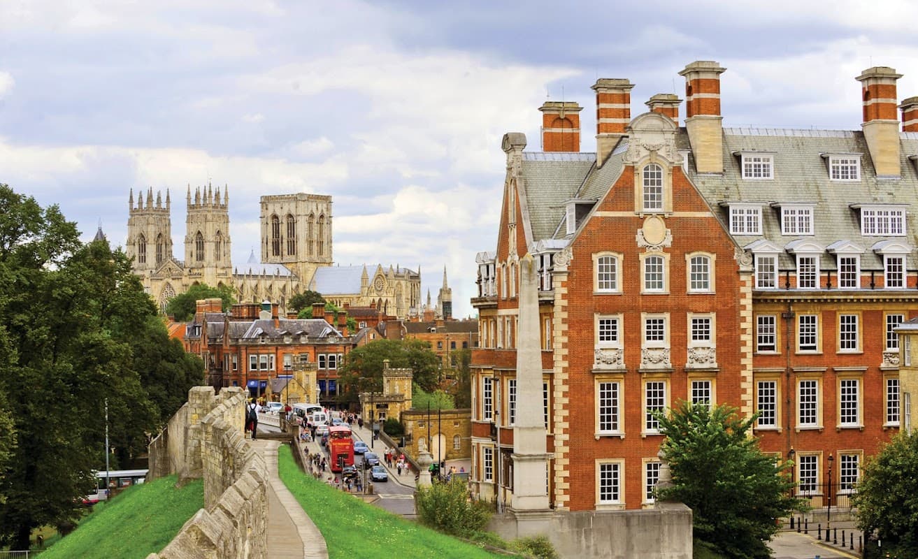 Red-brick hotel with ornate architecture, surrounded by greenery and historic city walls, with York Minster in the background.