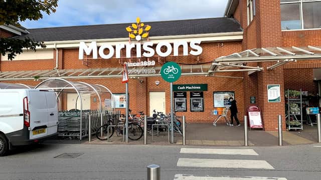 Morrisons grocery store entrance with bike racks, cash machines, and shopping carts outside.