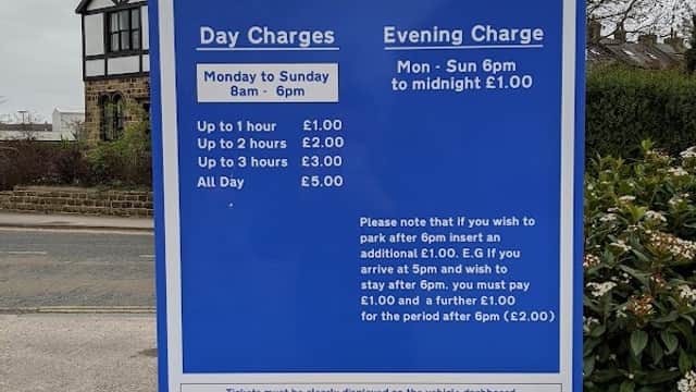 Sign for Wharfe View Car Park detailing parking charges and hours, with nearby buildings and trees in the background.