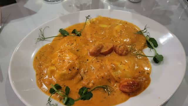 Plate of ravioli in a creamy tomato sauce, garnished with herbs and cherry tomatoes, on a white tablecloth.