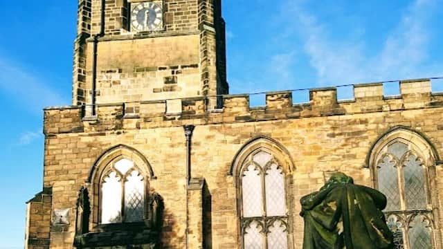Historic stone church with a tall clock tower and arched windows, surrounded by green grass under a blue sky.