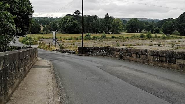 View of a quiet road leading to Summerbridge Stores Ltd, surrounded by greenery and a cloudy sky.