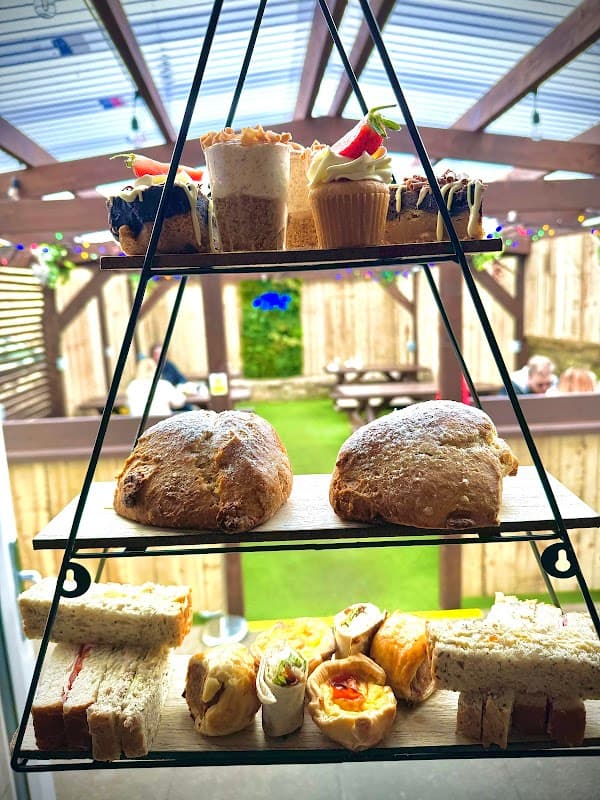 Tiered stand displaying an assortment of cakes, pastries, and sandwiches, set in a cozy outdoor tearoom.