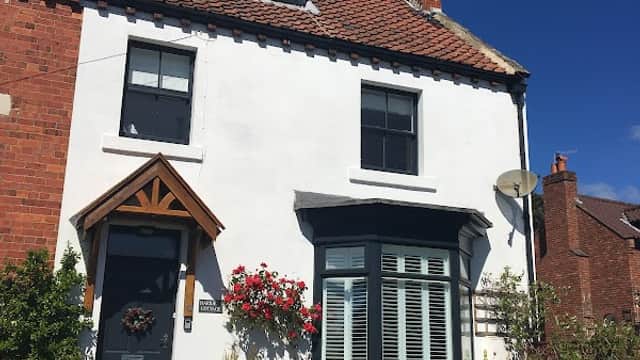 White and red brick cottage with a wooden door, flower-filled garden, and blue sky in Briggswath, Yorkshire.