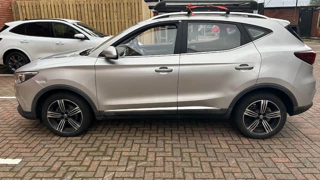 Silver SUV parked in a Pay & Display car park with brick paving and a wooden fence in the background.
