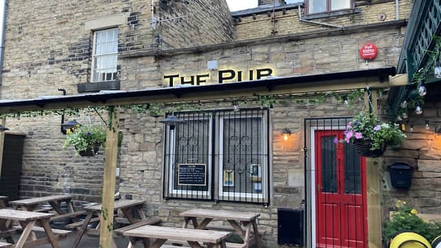 Stone exterior of a pub with a red door, outdoor seating, and hanging flower baskets in Chiserley, Yorkshire.