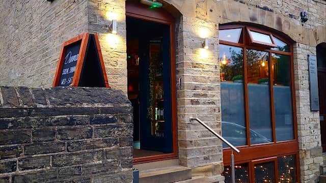 Stone building entrance with a blue sign reading "Denman's," illuminated by wall lights and featuring a staircase.