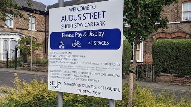 Welcome sign for Audus Street Short Stay Car Park, detailing payment and parking information, surrounded by greenery.