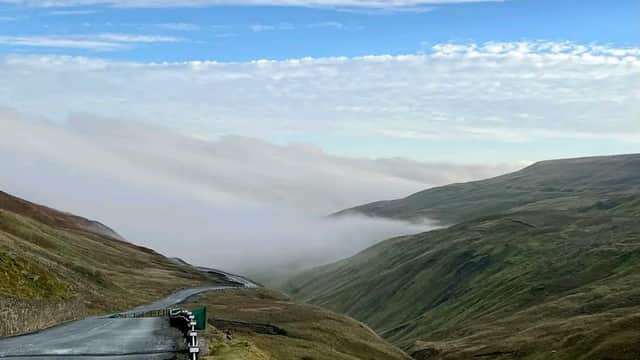 Scenic view of Buttertubs Pass with winding road, rolling green hills, and misty valleys under a cloudy sky.