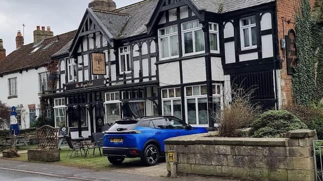 Tudor-style building with black and white facade, parked blue car, and outdoor seating in front.