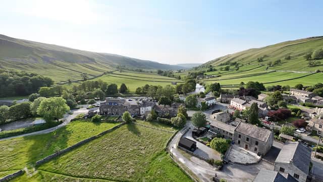 Aerial view of Kettlewell village, lush green hills, stone buildings, and winding river under a clear blue sky.