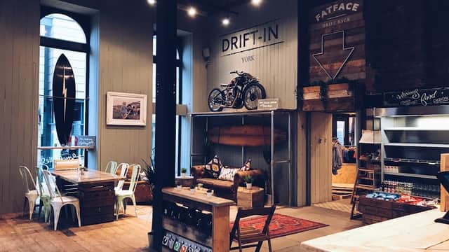 Cozy cafe interior with wooden floors, surfboards, a vintage motorcycle, and rustic furniture.