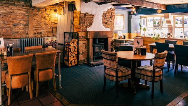 Cozy restaurant interior with stone walls, wooden beams, a fireplace, and tables set with chairs in warm tones.
