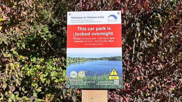 Sign indicating car park hours, surrounded by greenery and trees, with a scenic lake in the background.