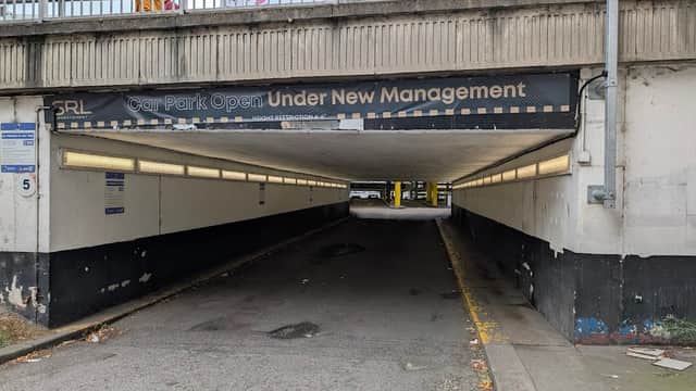 Multi-storey car park entrance with "Car Park Open Under New Management" sign and dimly lit tunnel.