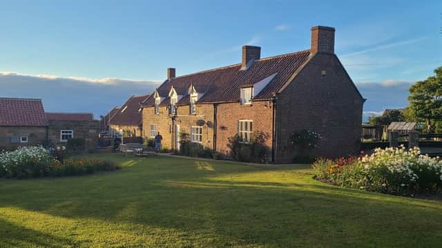 Quaint brick hotel surrounded by lush gardens and flower beds under a clear blue sky in Low Hawsker, Yorkshire.