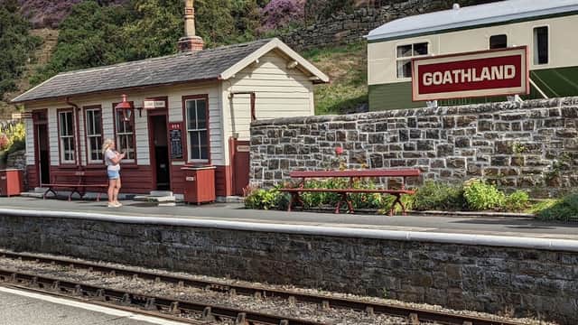 Levisham Station with a quaint building, picnic table, and a sign for Goathland amidst purple heather-covered hills.