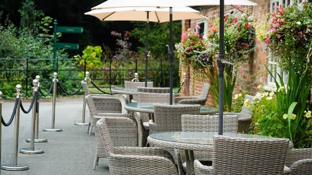 Outdoor seating area at Miss Daisy's Tea Rooms with wicker chairs, tables, and umbrellas, surrounded by flowers.