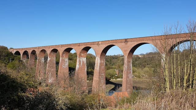 Red brick viaduct arches over a lush valley under a clear blue sky in Ruswarp, Yorkshire.