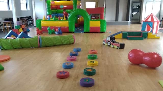 Brightly colored inflatable play equipment in a spacious hall, decorated with bunting and soft play areas.
