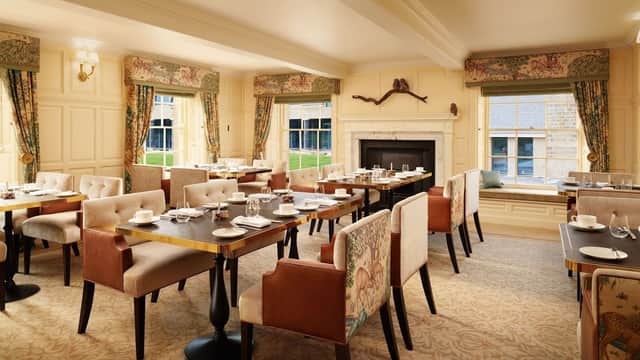 Elegant cafe interior with wooden tables, plush chairs, and large windows, featuring a cozy fireplace and tasteful decor.