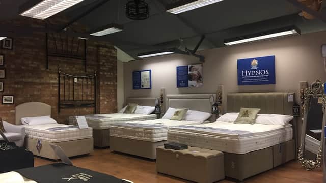 Showroom featuring various stylish beds and mattresses, with a brick wall backdrop and modern lighting.