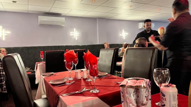 Tables with red and white tablecloths set for dining, featuring wine glasses and red napkins, in a lively restaurant setting.