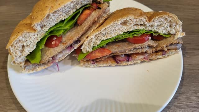 A plate with a sliced sandwich filled with lettuce, tomatoes, and a meat substitute on whole grain bread.