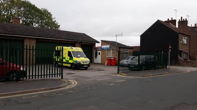 Ambulance station with a parked ambulance, nearby cars, and a gated entrance in a residential area.