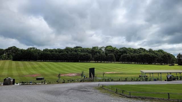 Green shooting grounds with neatly trimmed grass, trees in the background, and a cloudy sky overhead.