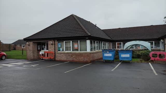 Stillington Surgery building with a sloped roof, parking area, and recycling bins outside on a cloudy day.