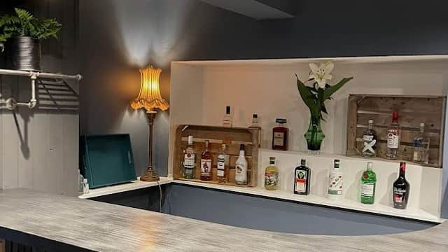 Modern bar area featuring a curved counter, various bottles, a lamp, and decorative plants.