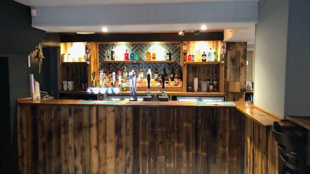 Wooden bar with a variety of drinks displayed on shelves, modern decor, and patterned floor tiles.