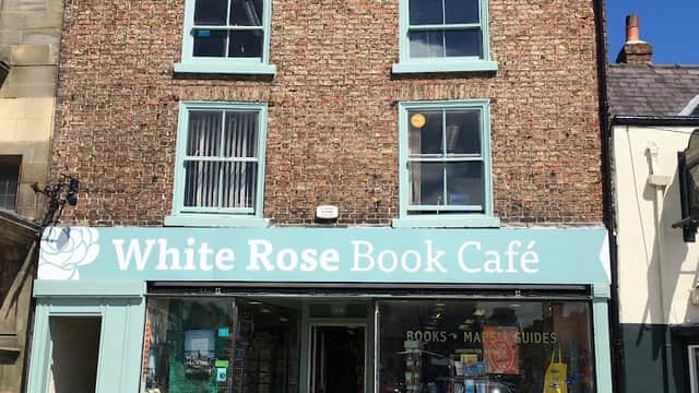 Charming brick building with a teal sign for White Rose Book Café, featuring books displayed in the window and a clear blue sky.