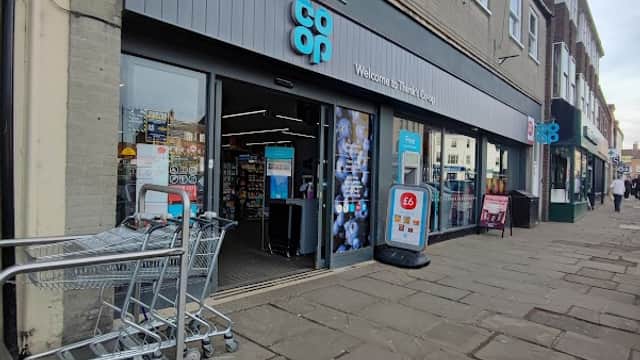 Co-op Food store entrance in Thirsk, featuring shopping carts and signage on a stone-paved market street.