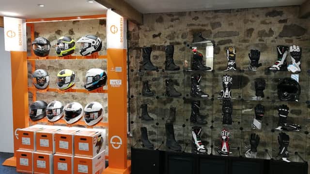Display of motorcycle helmets and gear, including gloves and boots, in a shop with stone walls and orange accents.