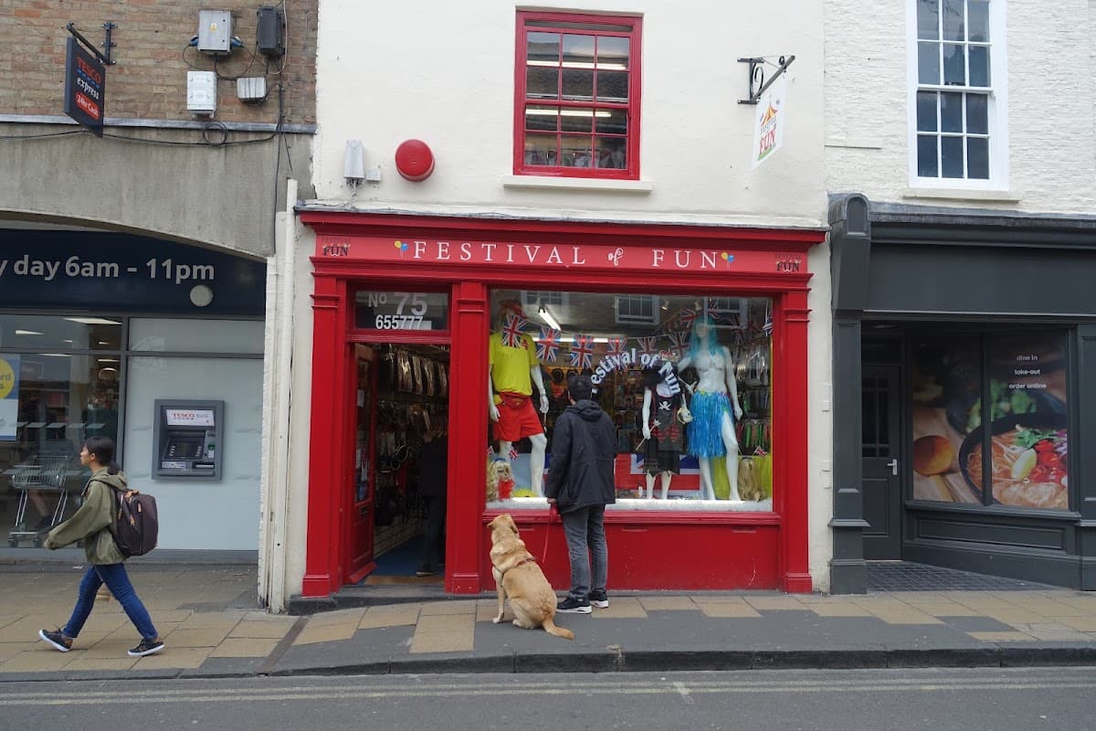 Bright red storefront labeled "FESTIVAL OF FUN," featuring colorful clothing displays and a dog outside.