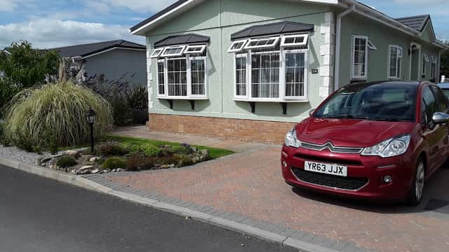 Green hotel building with large windows, landscaped garden, and a red car parked on a brick driveway.