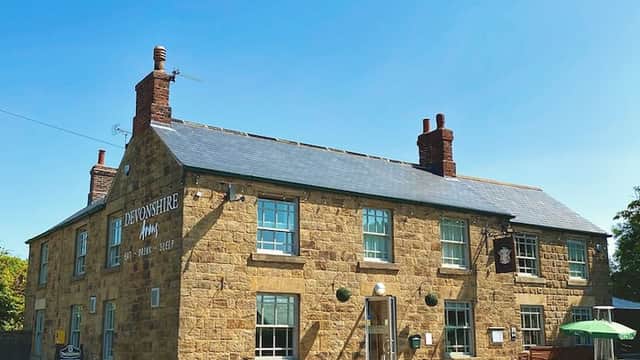 Historic stone inn with green-framed windows, brick chimneys, and outdoor seating under a clear blue sky.
