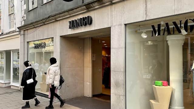 MANGO clothing store entrance in York, with shoppers and large windows displaying merchandise.
