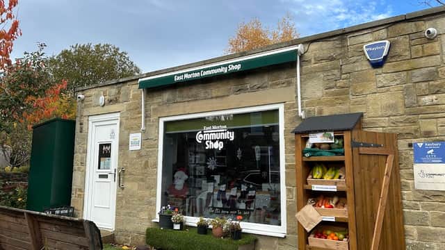 East Morton Community Shop with stone exterior, green awning, display of produce, and festive decorations in window.
