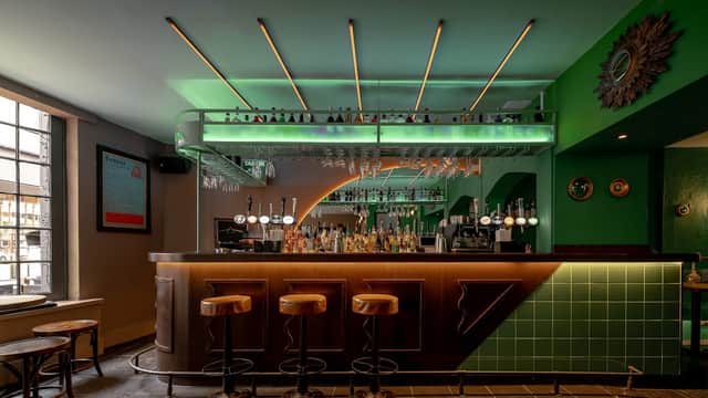 Stylish bar with a green and wooden interior, illuminated shelves, and bar stools against a modern backdrop.