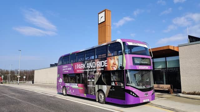 Double-decker bus at Stourton Park & Ride, modern building with a clock tower, clear blue sky in the background.