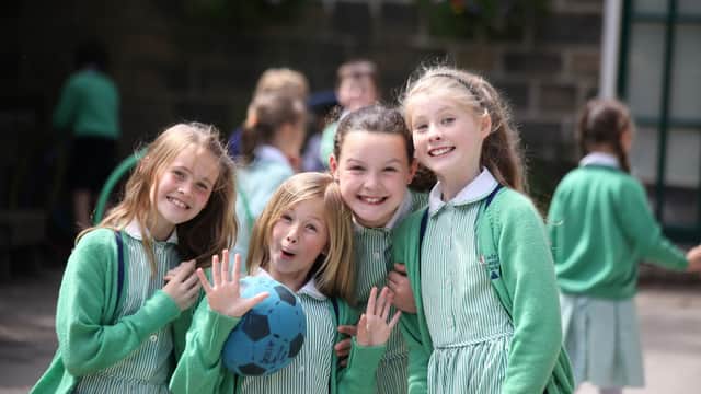 Four smiling girls in green cardigans and striped dresses, holding a blue ball, enjoying time at Lady Lane Park School.