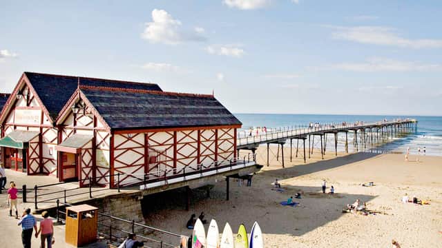 Victorian-style building by the beach, with a pier extending into the sea and surfers' boards lined up in the foreground.