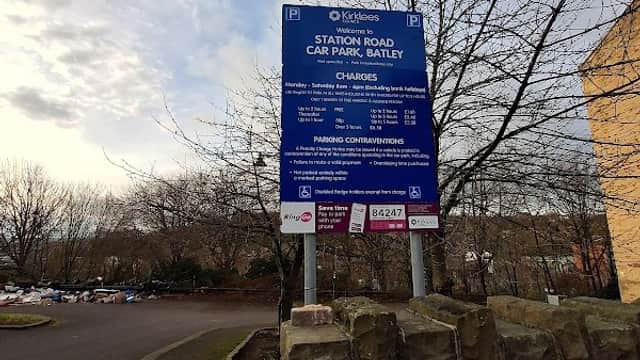 Sign for Station Road Car Park in Batley, detailing parking charges and regulations, surrounded by trees and a stone wall.