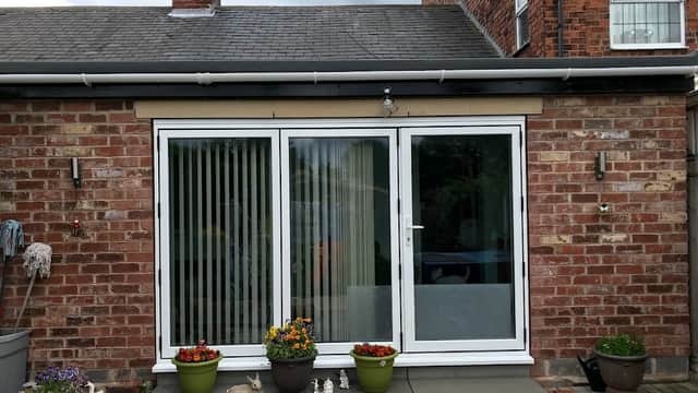 Brick building with sliding glass doors, potted plants, and a patio area. Cloudy sky in the background.