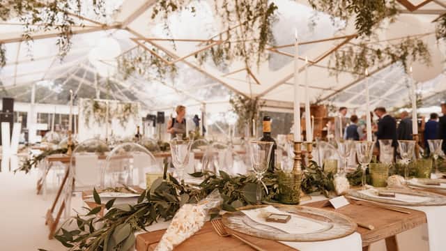 Elegant event setup with long wooden tables, greenery, candles, and a clear marquee, creating a festive atmosphere.